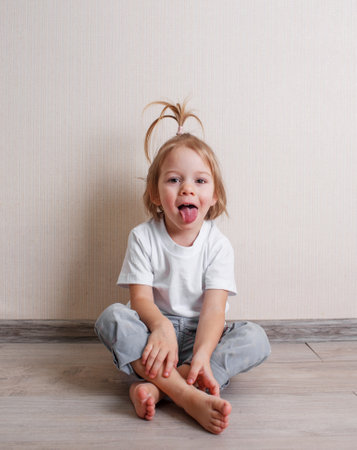 a little beautiful girl sits at home on the floor near the wall and makes funny facesの写真素材