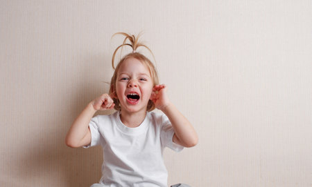 a little beautiful girl sits at home on the floor near the wall and makes funny facesの写真素材