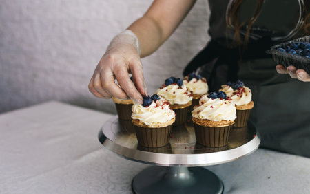 the chef girl decorates fresh cupcakes covered with vanilla cream with berries.Sweet homemade cupcakes with cream on a tray. Food for breakfast. Freshly baked cupcakes for dessert.の写真素材