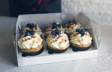 A girl cook in a gray apron packs cupcakes with cream in a gift box to send the order to the customer.の写真素材