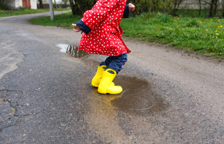 A little girl in yellow boots jumps on spring puddles, close-up. Happy childhoodの写真素材
