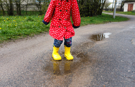 A little girl in yellow boots jumps on spring puddles, close-up. Happy childhoodの写真素材