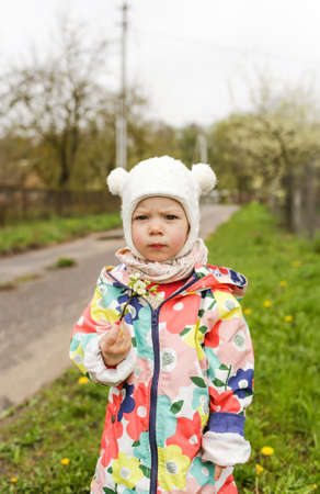 a little girl in a bright jacket stands outside in the spring and holds a branch with spring white flowers in her hands.の写真素材