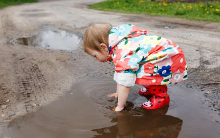 a little girl in a bright jacket and rubber boots happily plays in a spring puddle. Children's happiness.の写真素材