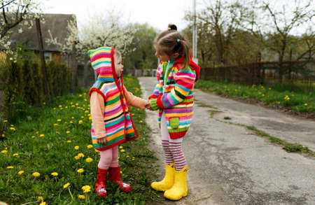 two little girls in bright clothes hold each other's hands among the yellow dandelions. Happy childhood.の写真素材
