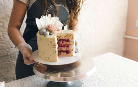 a pastry chef in a gray apron puts a large cake on a stand.の写真素材