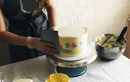 A young pastry chef girl in a gray apron decorates a cake in the kitchen