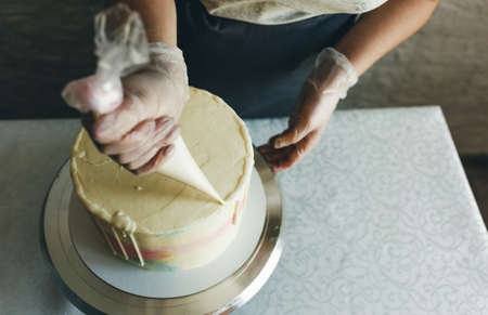 A pastry chef girl makes a wedding cake with her own hands and squeezes the cream on the layers of the cake. A pastry chef makes a pink cream using a cooking spatula. Put the cream on the cakeの写真素材