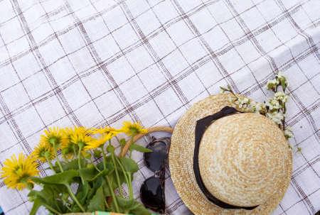 A bouquet of yellow flowers sunglasses and a straw hat sakura branches lie on the tablecloth. Top view.の写真素材