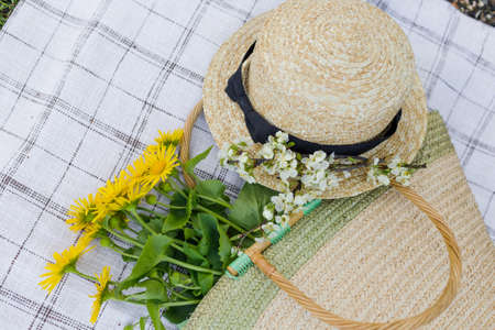 A bouquet of yellow flowers a straw hat and a straw bag lie on the tablecloth. Top view.の写真素材