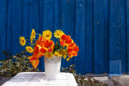 a bouquet of spring flowers in a white vase on a blue wooden background.の写真素材