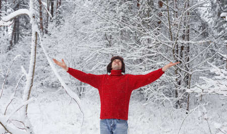 A man in a red sweater stands in a snow-covered forest with his hands in the air. Family winter vacationの写真素材