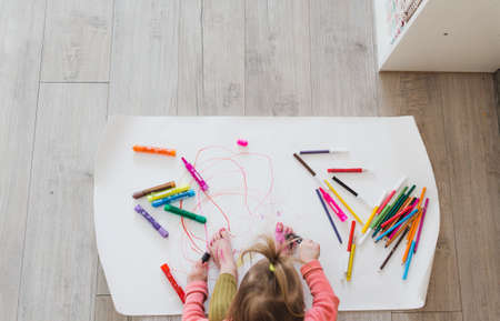 A little girl, sitting on the floor, enjoys creativity, drawing pictures with pencils on paper. top viewの写真素材