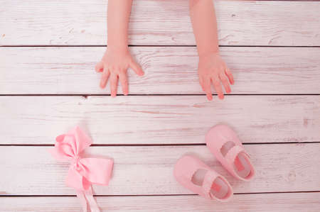 baby's hands reach for a pink bow and pink slippers on a wooden background, top viewの写真素材