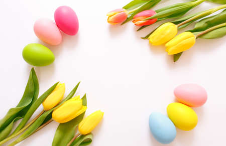 Beautiful yellow tulips and colorful Easter eggs on a white background, top view.の写真素材