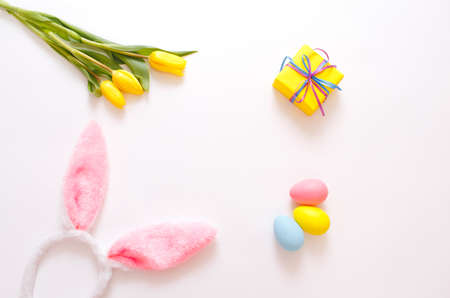 yellow tulips and colorful Easter eggs gift box, rabbit ears on a white background, top viewの写真素材
