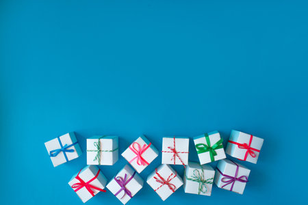 Many white boxes with colored ribbons lie on a blue background. Top view. Space for the text.の写真素材