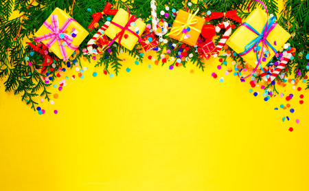 pine branches and colorful gift boxes, confetti on a yellow background top view. Space for the text.の写真素材