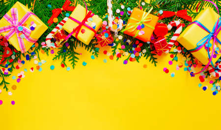 pine branches and colorful gift boxes, confetti on a yellow background top view. Space for the text.の写真素材