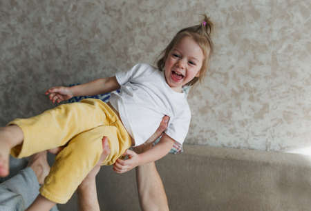 dad plays with his daughter on the couch and lifts her high up in his arms.の写真素材
