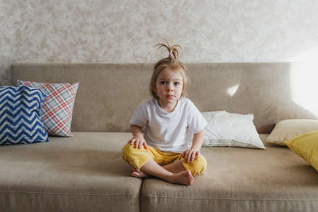 a little girl sits at home on the couch with a thoughtful look.の写真素材