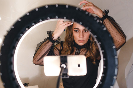 A girl blogger tells how to do her hair to her subscribers looking at the phone, in front of a large...
