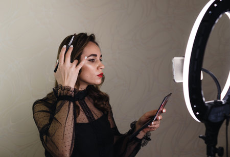 A beautiful blogger girl puts makeup on her face and shoots a video on her phone for her viewers.