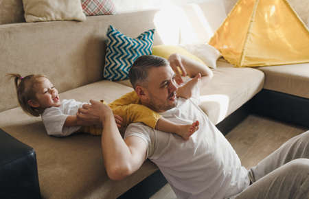 Happy dad plays on the couch with his daughter, laughs and enjoys spending time with pleasure.の写真素材