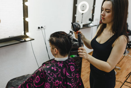 a girl hairdresser makes a hairstyle for a woman client in a modern beauty salon.の写真素材
