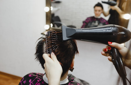 a girl hairdresser makes a hairstyle for a woman client in a modern beauty salon.の写真素材