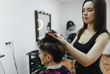 a girl hairdresser makes a hairstyle for a woman client in a modern beauty salon.の写真素材