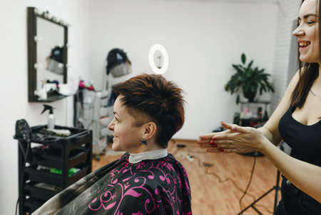 a girl hairdresser makes a hairstyle for a woman client in a modern beauty salon.の写真素材