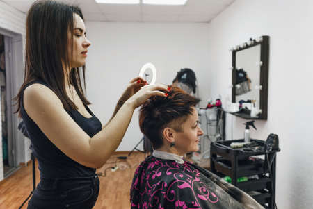 a girl hairdresser makes a hairstyle for a woman client in a modern beauty salon.の写真素材