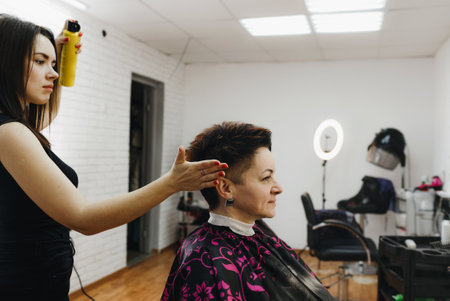 a girl hairdresser makes a hairstyle for a woman client in a modern beauty salon. Hair treatment with varnish.の写真素材