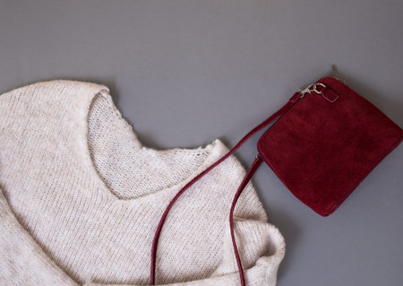 women's sweater, red velvet bag on gray background top view place for text