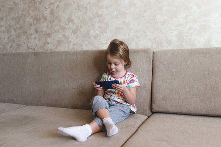 a little girl sits on the couch and looks at the phone.の写真素材