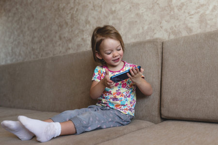 a little girl sits on the couch and looks at the phone.