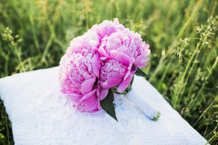 a large bouquet of pink peonies lies on a white pillow sunny summer