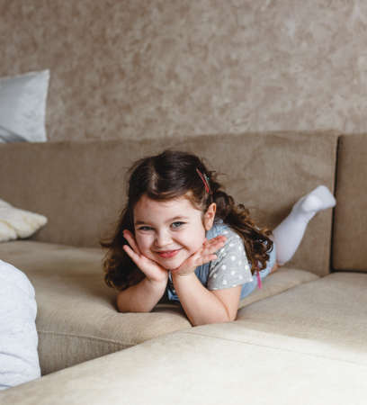a small beautiful girl lies on the sofa with her hands under her head and smilesの写真素材