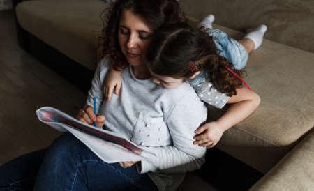 a little girl lies on the sofa next to her mother and watches as her mother draws drawings in an albumの写真素材