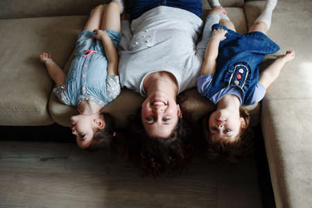 a young mother and two young daughters are lying on the sofa upside downの写真素材