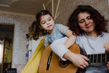 mom and daughters learn to play the guitar at home sitting on the couchの写真素材