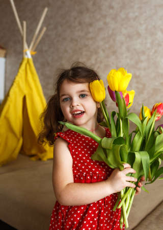 a little girl in a bright red dress holds a large bouquet of colorful tulipsの写真素材