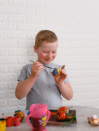 a boy paints eggs with colored paints to celebrate the Easter holiday