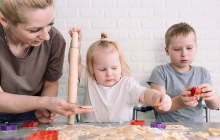 little girl and boy help mom in the kitchen to cook delicious cookies