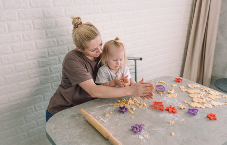 happy young mother and her little daughter together prepare delicious cookies sitting at the table...