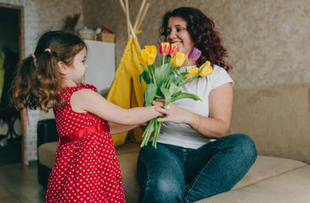 a little girl in a red dress gives a happy mother a large bouquet of bright tulips. A gift for parents.の写真素材