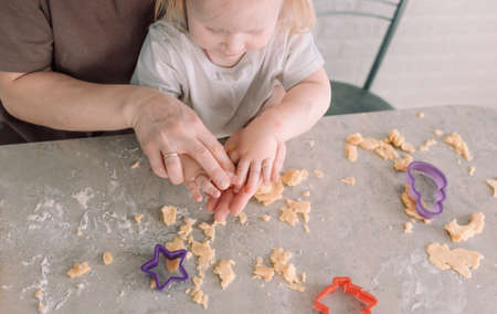 happy young mother and her little daughter together prepare delicious cookies sitting at the table in the home kitchenの写真素材