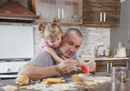 a happy dad and his little daughter cook cookies together in the kitchen. joint cooking, family valuesの写真素材