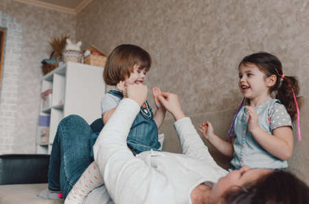 loving mom plays with her daughters lying on the couchの写真素材